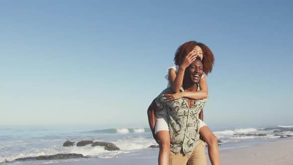 African American man carrying his wife on his back at beach