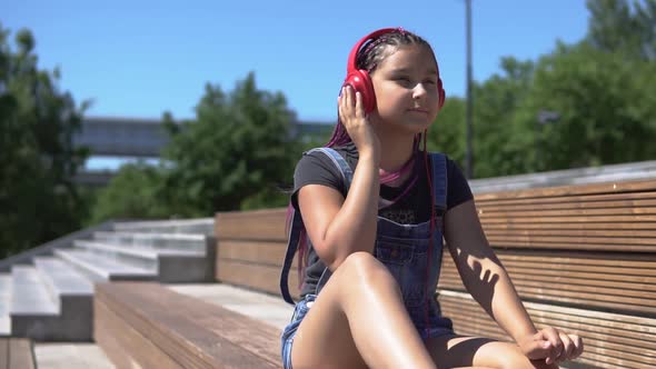 The Girl Listens to the Music on the Headphones Saddle on the Bench in the Park