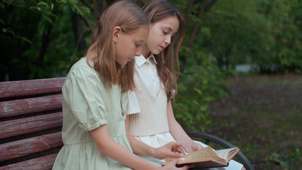 Two School Girls Reading Book Together in Park