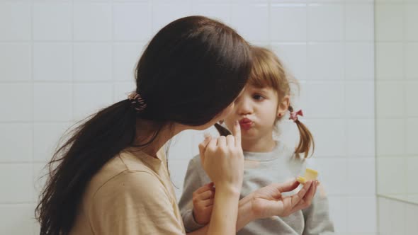 Cheerful mom smearing lip balm on daughter's lips