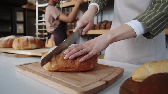 Woman Cutting Loaf of Bread in Bakery