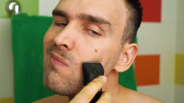 A Caucasian man shaves with an electric razor trimmer at home in the bathroom