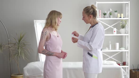 Professional Female Acupuncturist Showing Needles To Concentrated Caucasian Blond Woman. Side View