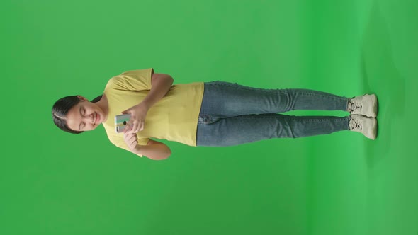 Full Body Of Smiling Kid Girl Use Mobile Phone And Pointing To Smart Phone In Green Screen Studio