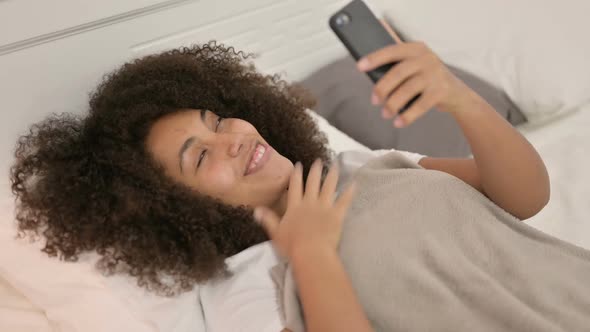 Video Chat on Smartphone By Young African Woman Laying in Bed