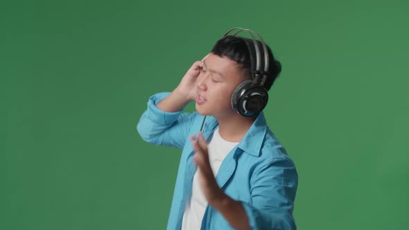 Side View Of Young Asian Boy Listening To Music With Headphones And Dancing In The Green Screen