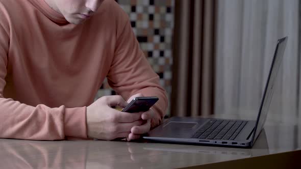 A young freelancer typing a message on his smartphone while working remotely.