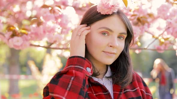 Caucasian teen girl smiling and looking into camera, blossom par full of cherry trees on a windy day