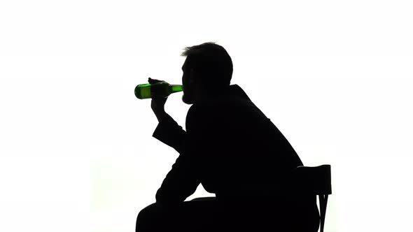 Alcoholic Sits with a Bottle in His Hands and Drinks. Side View. Silhouette White Background