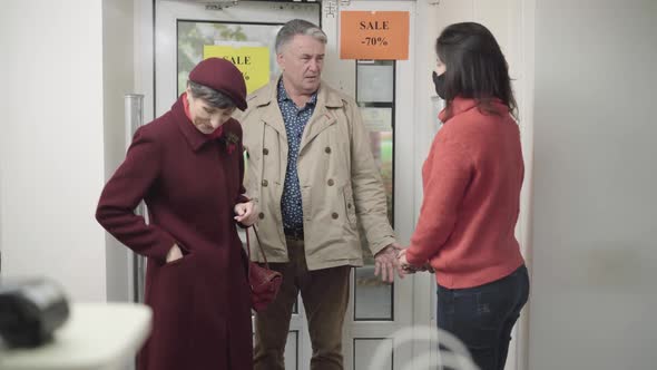 Shop Assistant Forcing Senior Couple To Put on Covid-19 Face Masks at Store Entrance. Woman Putting