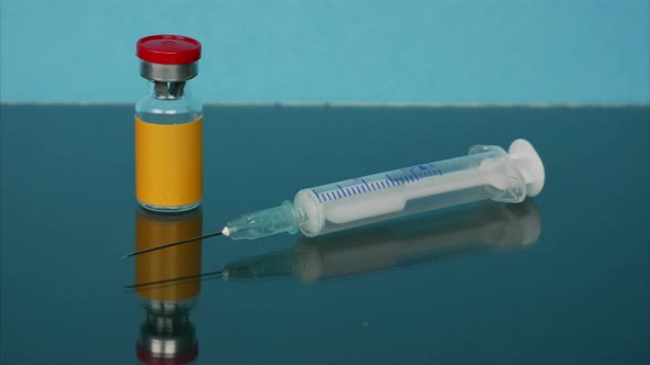 Transparent Medicine Bottle with Orange Label and Syringe Appear on Blue Background. Stop Motion