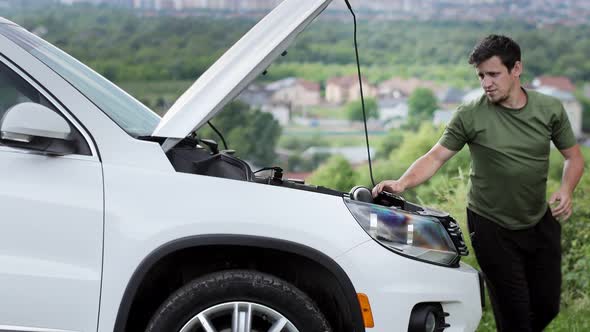 Young man standing near broken down car with popped up hood having trouble with her vehicle