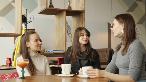 Three Girlfriends in a Cafe Are Talking and Drinking Their Beverages