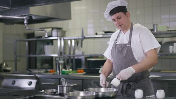 Medium Shot Confident Professional Cook in Chef Hat Pouring Water in Pan Frying Dinner in Restaurant