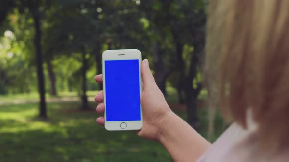 Close Up Young Female Hand Holding Smartphone with Blue Screen Chroma Key on Green Grass Background