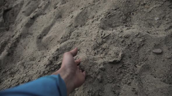 Man's hand taking sand between his fingers and then letting it fall