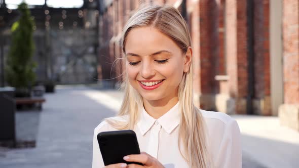 Portrait of Happy Blonde Woman Typing Message By Mobile Phone Outdoors