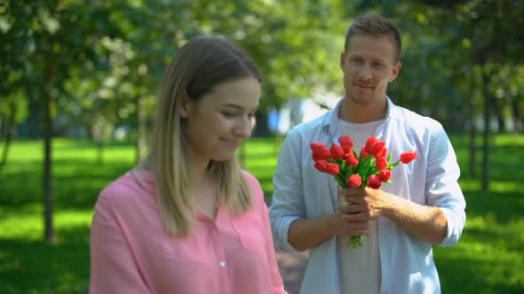 Happy Woman Smiling at Camera, Boyfriend With Flowers Behind, Date Invitation