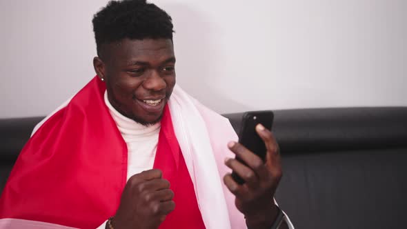 Young Happy Black Man with Polish Flag Watching Game Streaming on the Smartphone