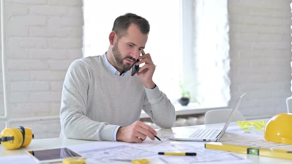 Young Architect with Documents Talking on Smartphone 