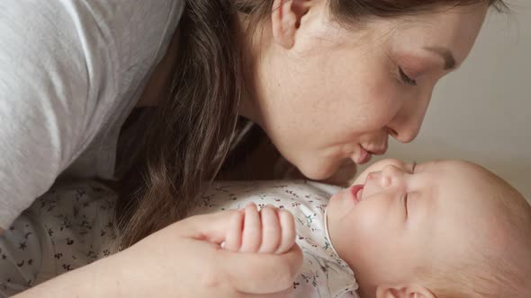 Young Mom Kisses Cheeks and Tiny Fingers of Baby Girl