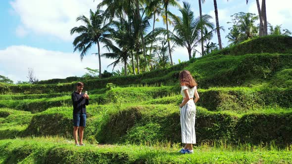 Laos, Asia. A man photographing his girlfriend using a smartphone. Pristine nature, romantic tropica