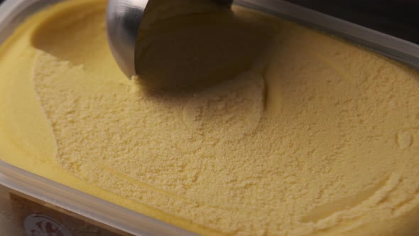 Close up view of a person scooping up fresh mango ice cream from tray.