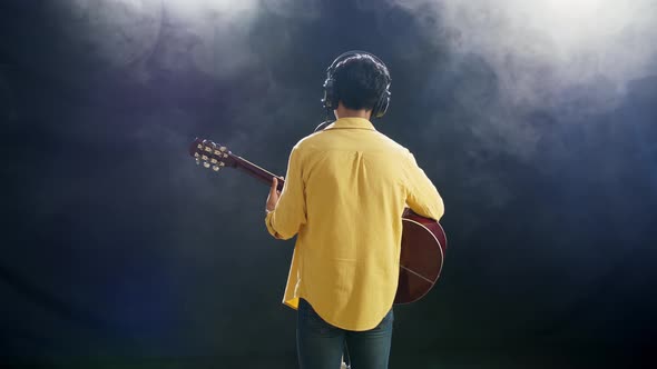 Young Boy With Headphone Playing A Guitar And Singing On The White Smoke Black Background