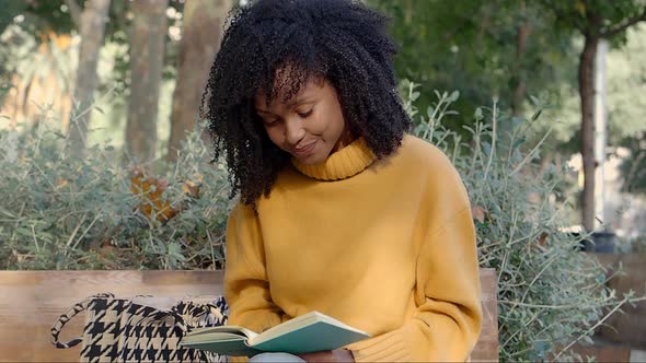 Smiling Brazilian Woman on a Bench Reading a Book Sitting on a Bench