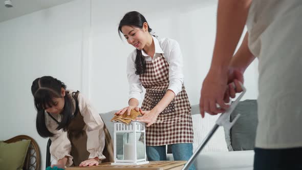 Asian lovely young family parents teaching their little kid daughter to clean living room in house.