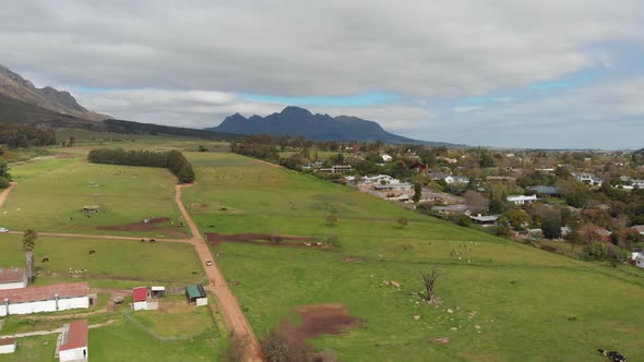 A drone shot sloly lowers over a farm. There is a residential area next to the farmland and mountain