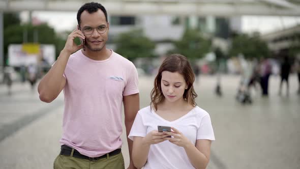 Front View of Two People Walking on Street with Smartphones