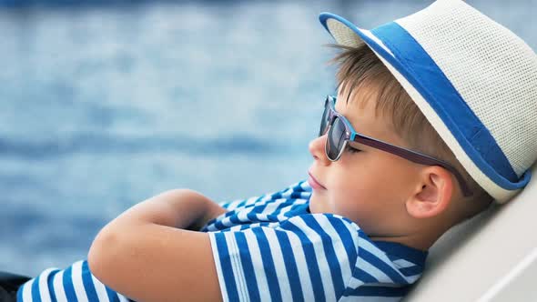 European Boy in Sunglasses and Hat Lying on Deck Chair Relaxing with Crossed Arms Showing Thumb Up