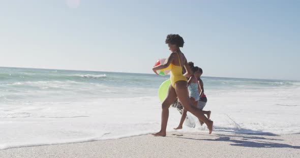 Smiling african american family with inflatables running on sunny beach