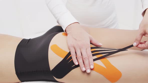 Therapist is applying kinesio tape to female body. Physiotherapy, kinesiology and recovery.