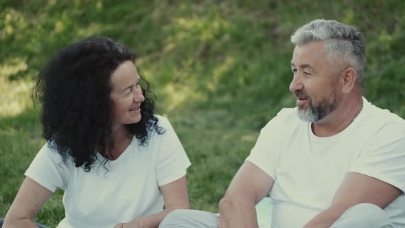 Senior Couple Man and Woman Looking at Each Other Sitting on the Grass