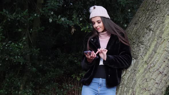 Young attractive woman in a park leaning against a tree in the winter time