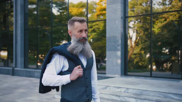 Handsome Bearded Mature Man in Suit Walking Outdoors on Modern Building Background During Sunny Day