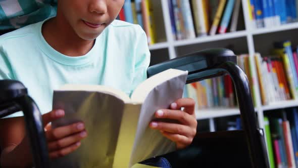 Disabled schoolboy reading book in library at school