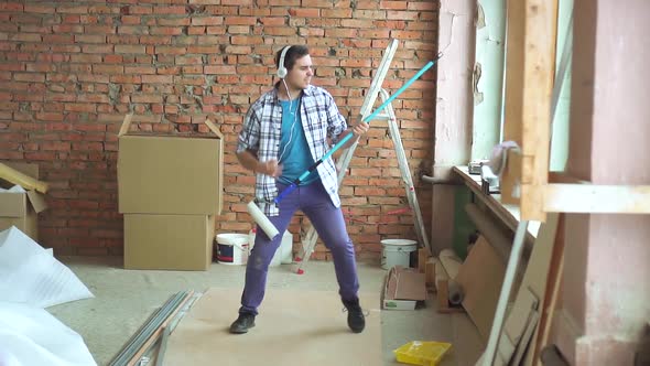 Joyful Male Builder in Shirt Plays on an Imaginary Guitar During the Repair