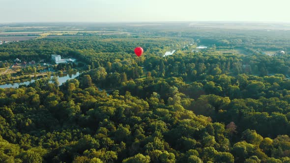 Aerial View of Red Hot Air Balloon Flies Over the Trees. Sunset Summer Scene