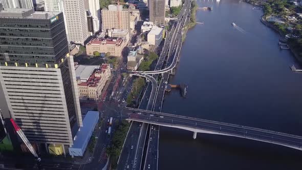 Aerial tilt shot of motorway with cars passing at base of city buildings along river Brisbane, Queen