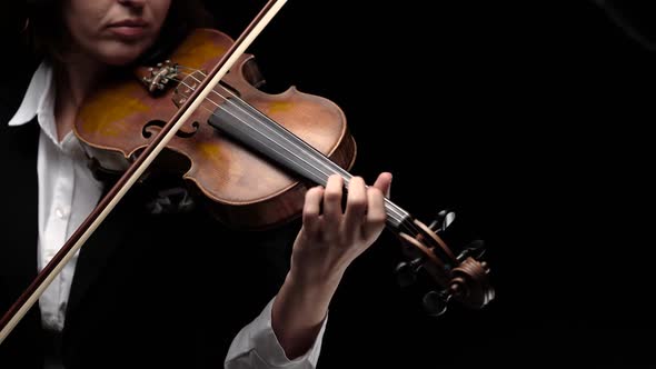 Girl Bows a Violin in a Dark Room. Black Background. Close Up