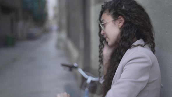 Long CurlyHaired Moroccan Girl Looking On Her Wristwatch While Talking On A Smartphone