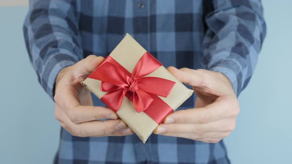 Wrapped in craft paper little gift box with tied red bow in hands