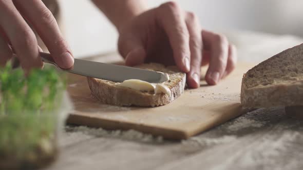 Male hands spread soft butter on slice of fresh rye bread. Bamboo cutting board. Slices of bread