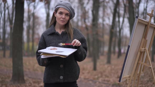 Portrait of Confident Attractive Young Woman Posing with Painting Palette in Autumn Park at Easel