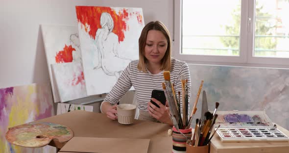 Young artist sitting in studio, checking smart phone
