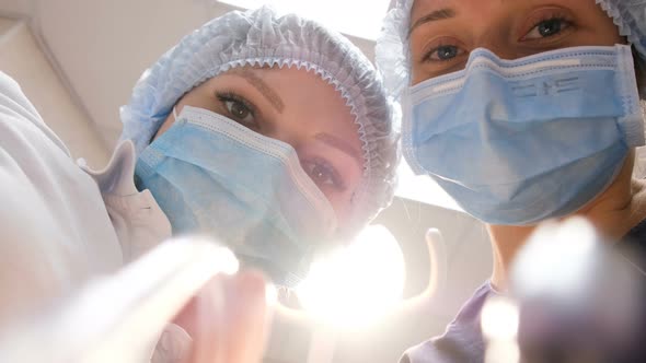 Smiling Dentist and the Assistant in Glasses Have Bent Over the Patient and Treat a Teeth