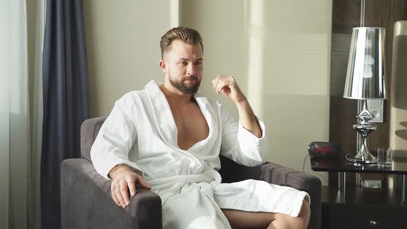 Thoughtful Bearded Male Sits on Couch in Hotel Room in the Morning